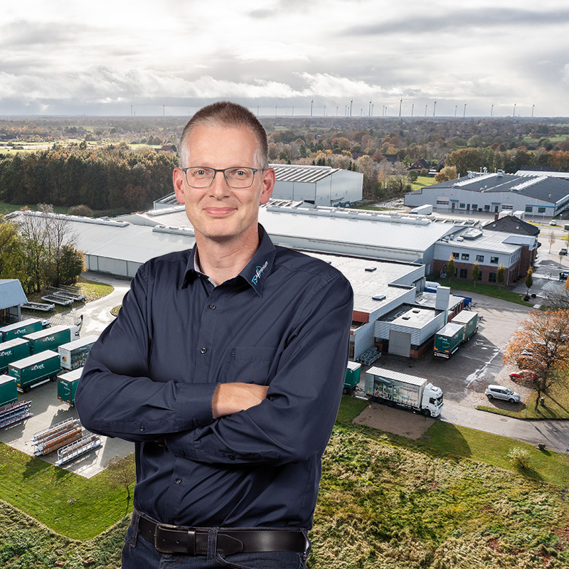 Person steht mit verschränkten Armen im Vordergrund und im Hintergrund ist ein Bild der TS Aluminium Hallen